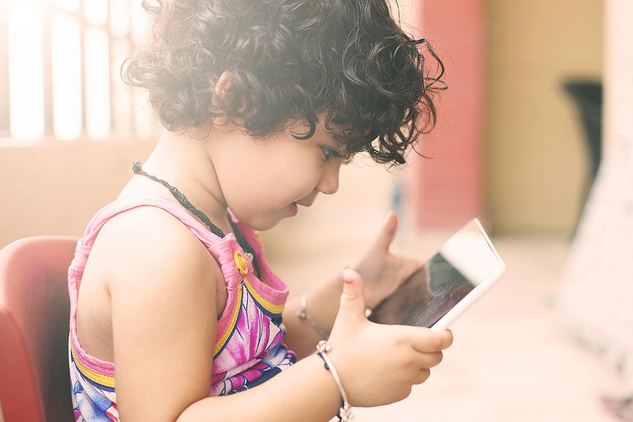 Cute small girl using a digital tablet in balcony Photograph by Triloks
