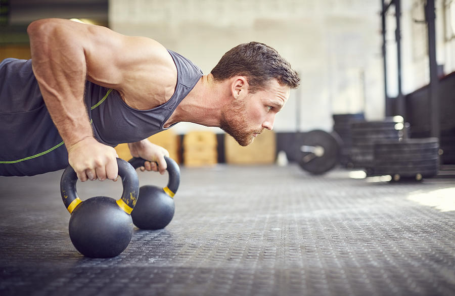 Determined athlete doing push-ups on kettlebells in gym Photograph by Neustockimages