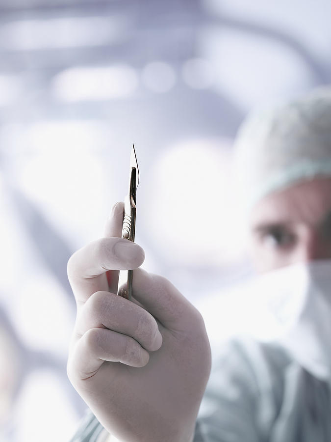 Doctor holding a scalpel in foreground Photograph by Chris Ryan