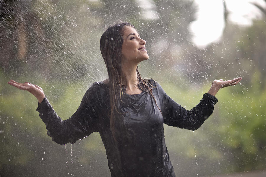 Drenched young woman with arms open in rainy park Photograph by Zero Creatives