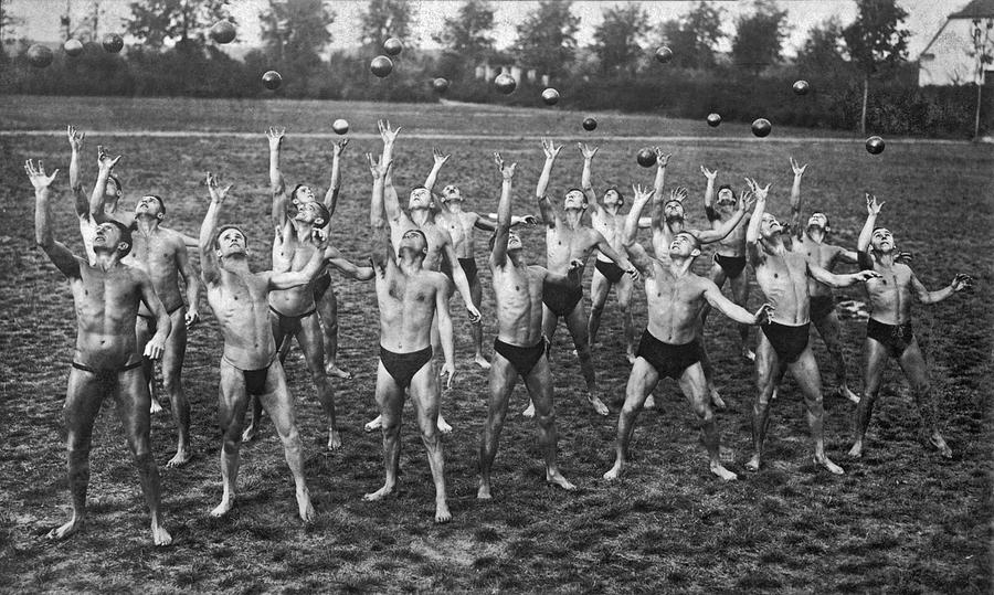 Black And White Photograph - Eighteen Men Tossing Balls by Underwood Archives