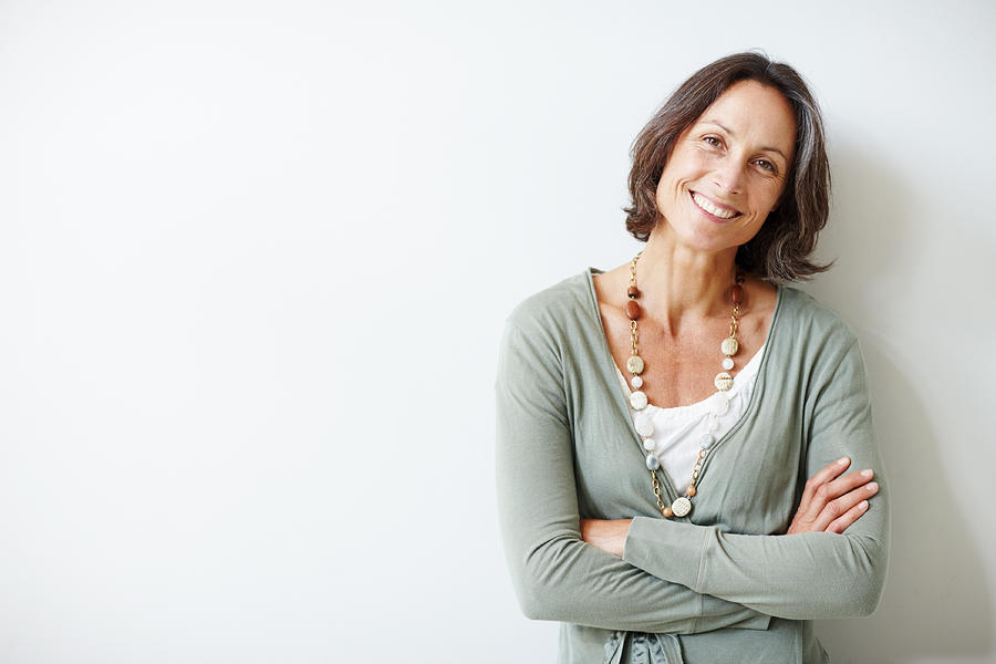 Elegant middle aged woman with her arms crossed against white Photograph by GlobalStock