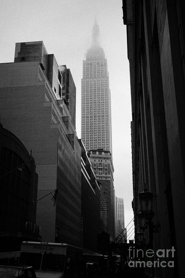 Winter Photograph - empire state building shrouded in mist in amongst dark cold buildings on 33rd Street new york city by Joe Fox