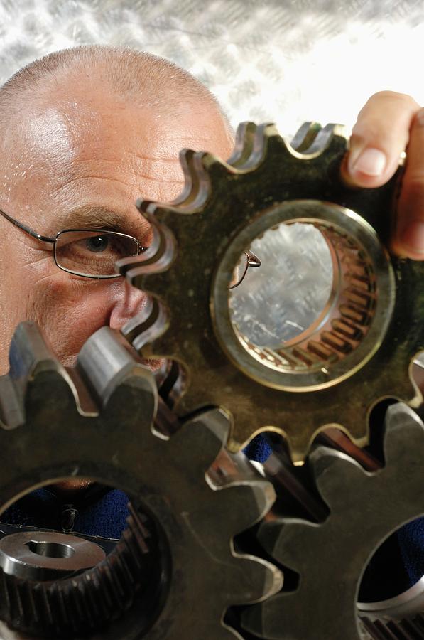 Engineer Scrutinising Metal Cogs Photograph by Christian Lagerek/science Photo Library