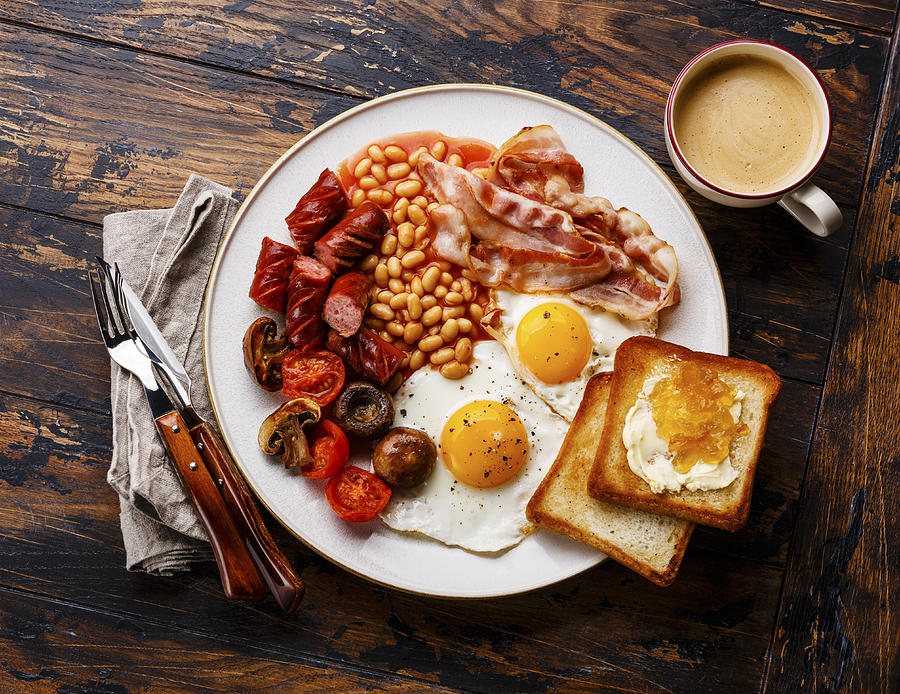 English breakfast with fried eggs, sausages, bacon, beans, toasts and coffee on wooden background Photograph by The Picture Pantry