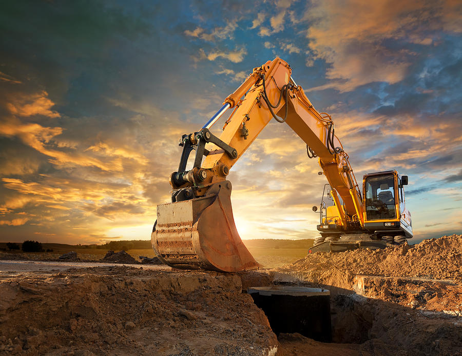 Excavator at a construction site against the setting sun. Photograph by Avalon_Studio