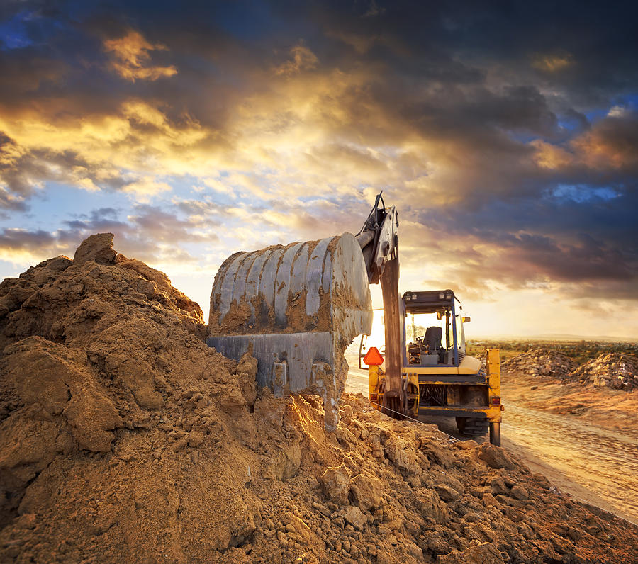 Excavator on the construction site of the road against the setting sun Photograph by Avalon_Studio
