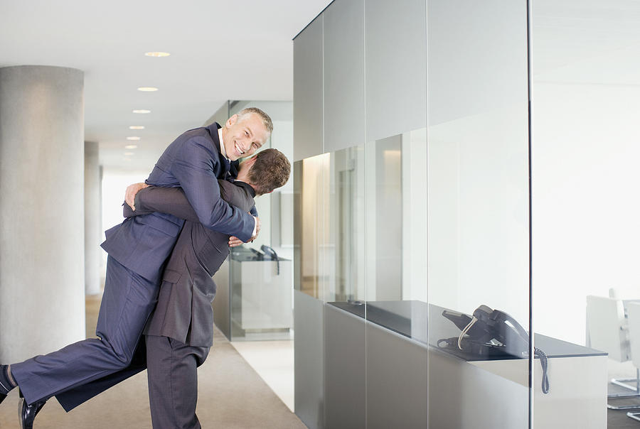 Excited businessman lifting co-worker in office corridor Photograph by Martin Barraud