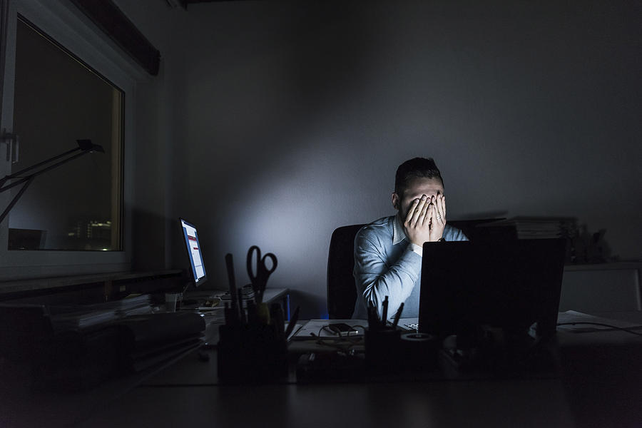 Exhausted businessman sitting at desk in office at night Photograph by Westend61