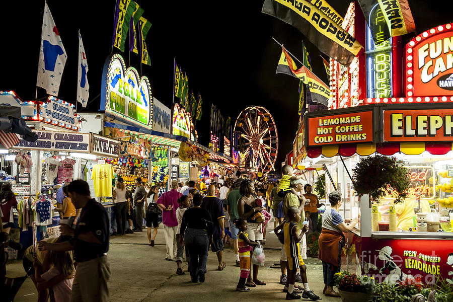 Fairgoers walk the midway at night at a county fair Photograph by William Kuta