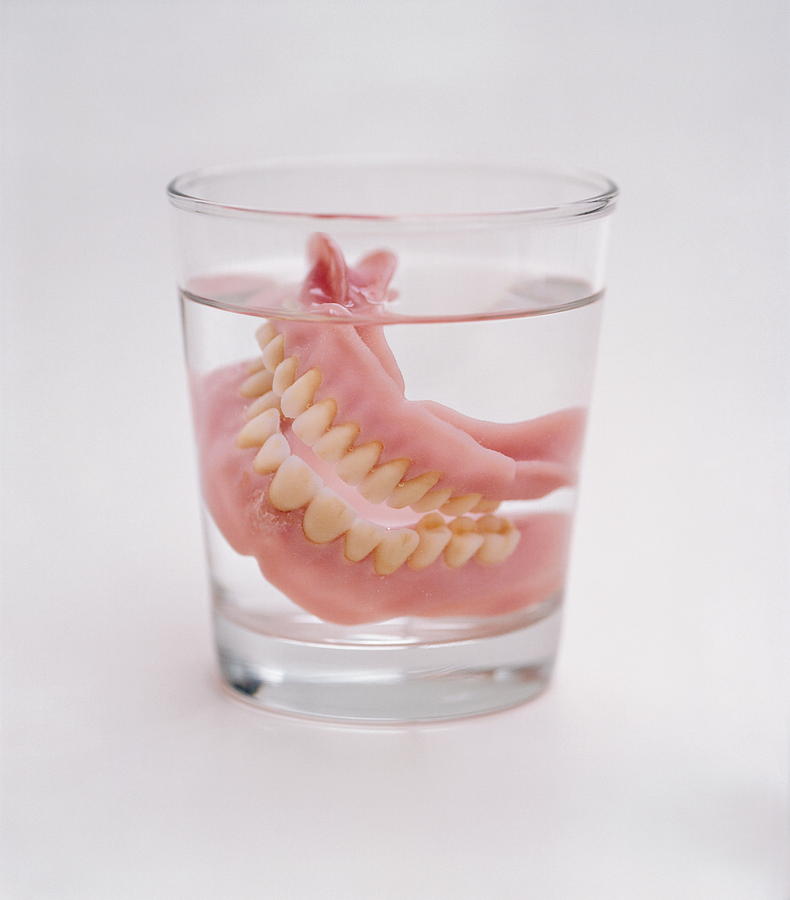 False teeth in glass of water, close-up Photograph by Christian Adams