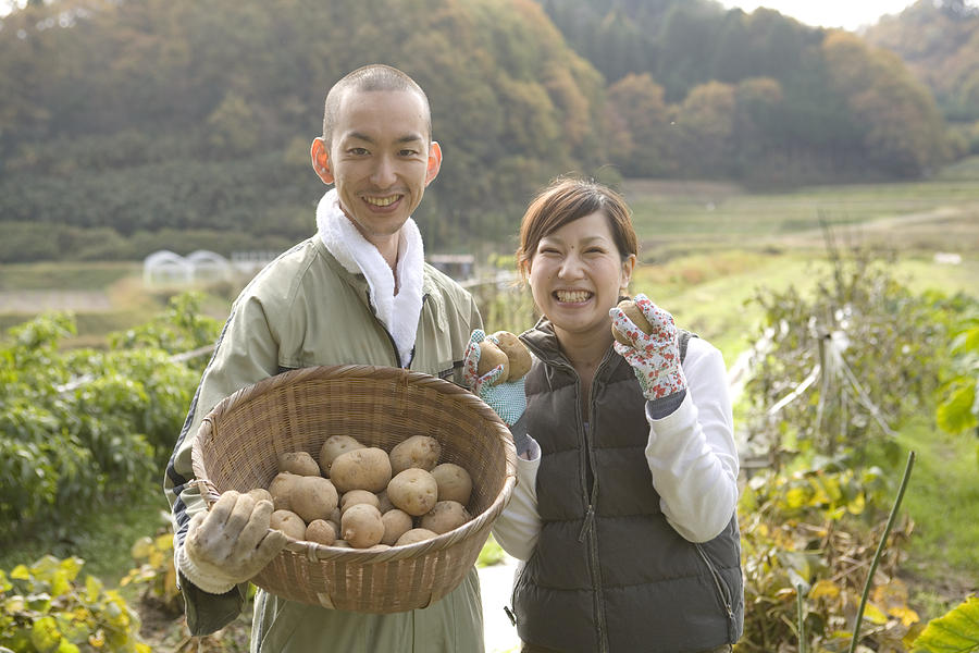Famer couple holding potatoes, smiling, portrait Photograph by Indeed