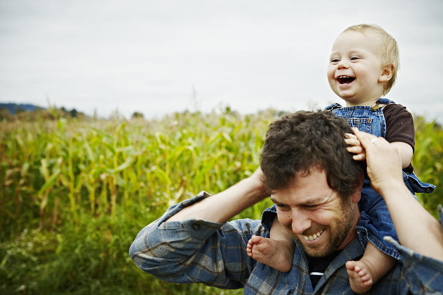 Farmer holding baby boy on shoulders laughing Photograph by Thomas Barwick