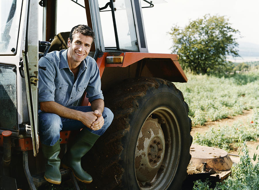 Farmer Sitting on a Tractor in a Field Photograph by Digital Vision.