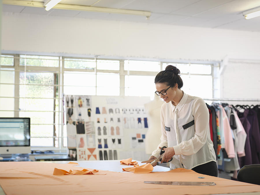 Fashion designer cutting cloth in fashion design studio Photograph by Monty Rakusen