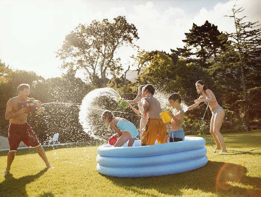 Father Aims a Water Gun at Children Throwing Water in a Paddling Pool Photograph by Digital Vision.