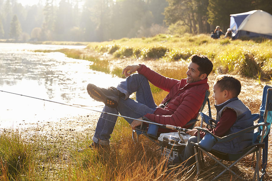 Father and son on a camping trip fishing by a lake Photograph by Monkeybusinessimages