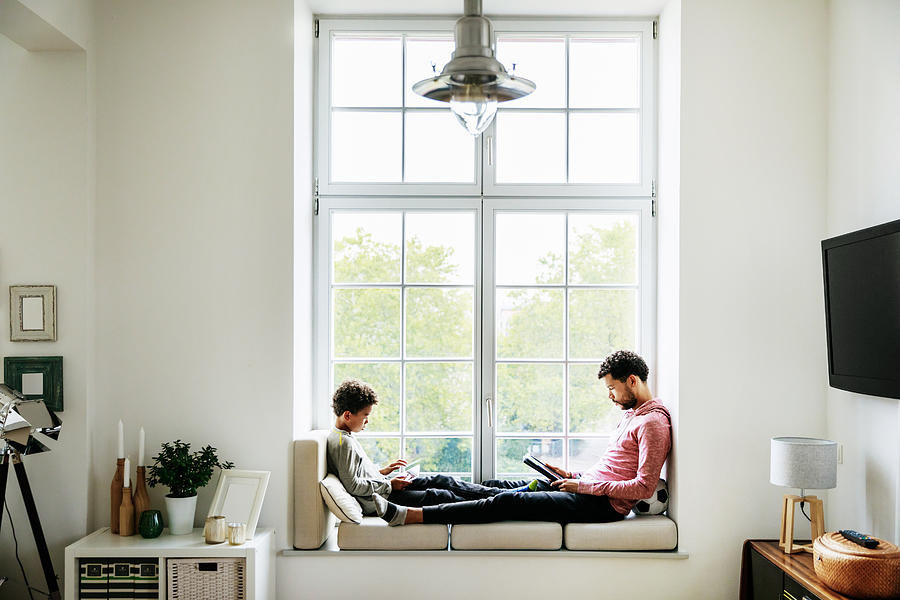 Father And Son Relaxing By Large Window At Home Photograph by Tom Werner