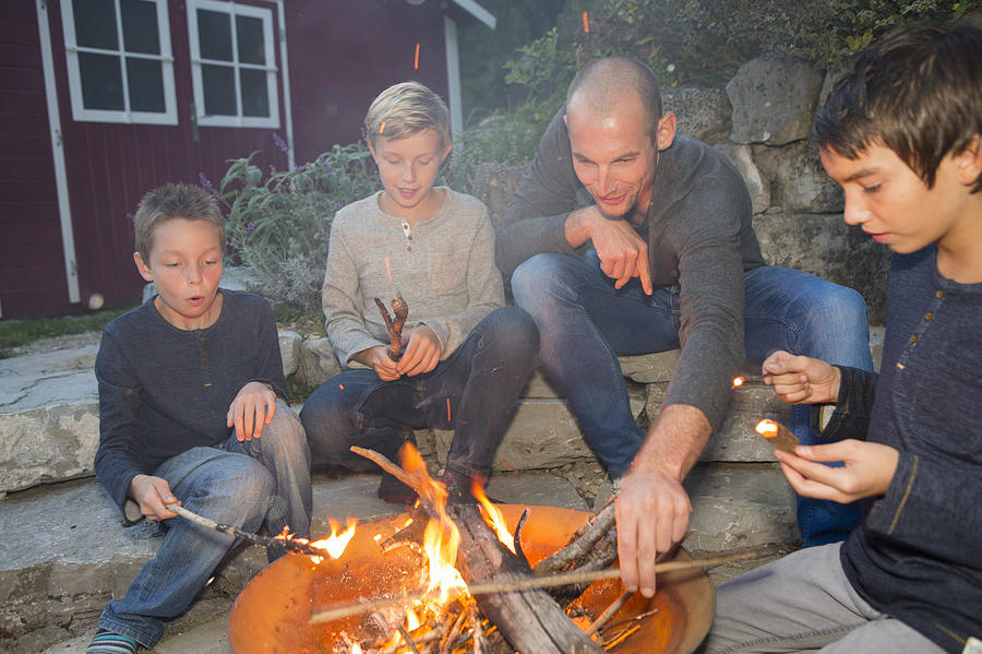 Father and three sons sitting by garden campfire at dusk Photograph by Judith Haeusler