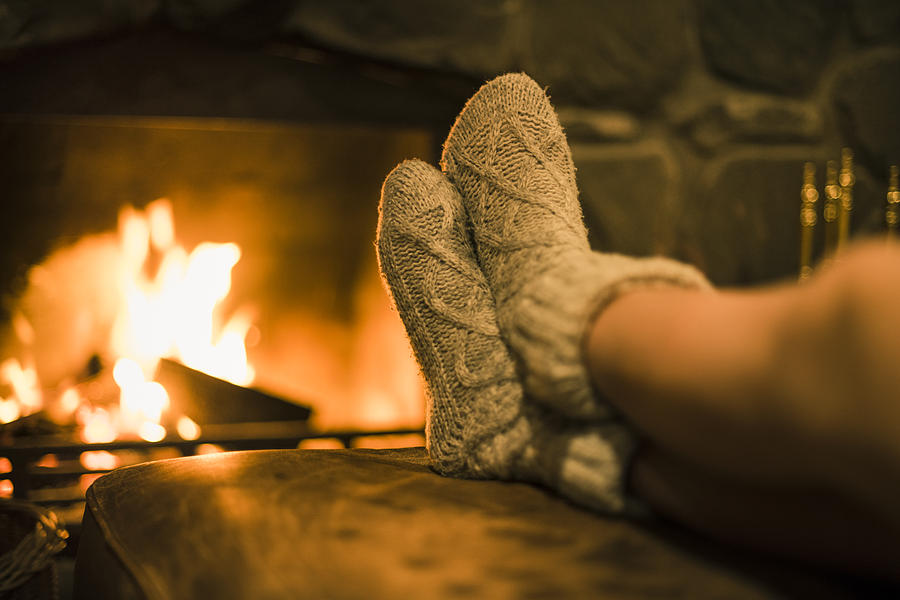 Feet in wool socks near fireplace Photograph by Johner Images