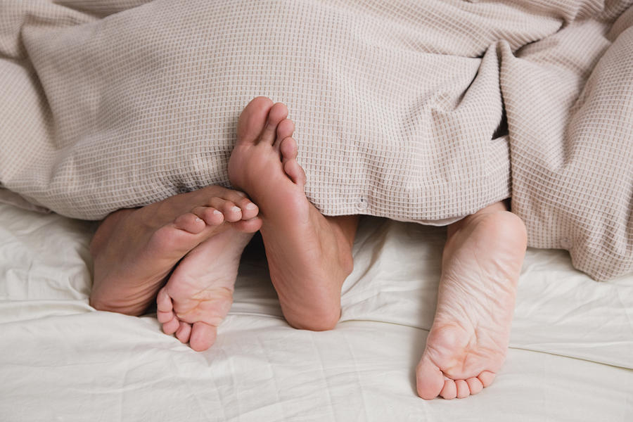 Feet under covers in bed Photograph by Vstock LLC