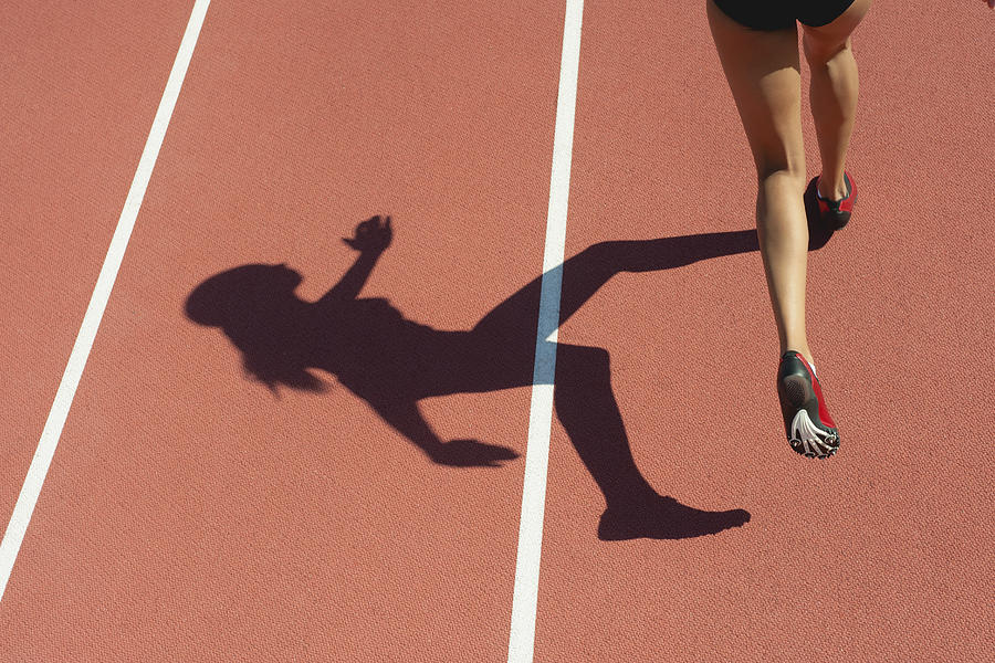 Female athlete running on track, low section, focus on shadow Photograph by PhotoAlto/Odilon Dimier