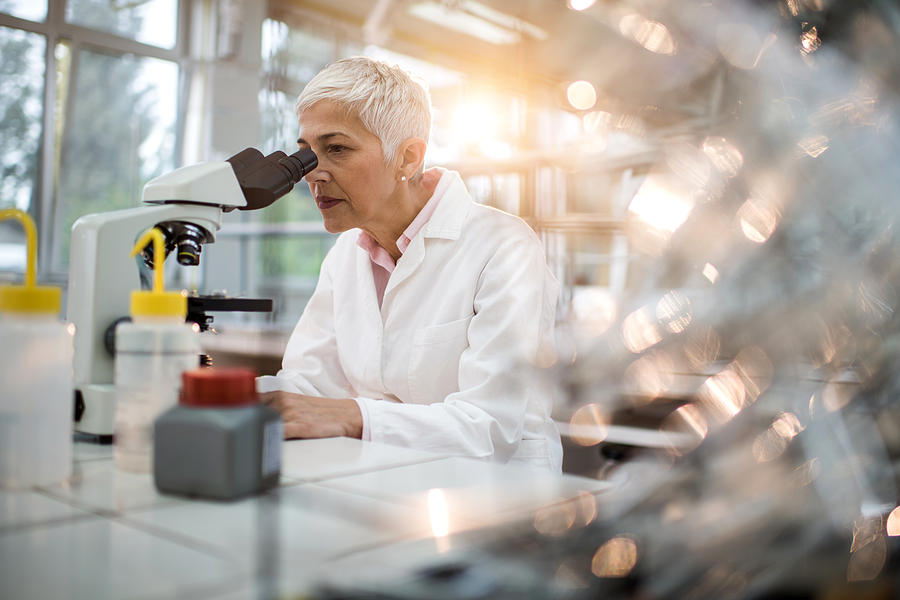 Female chemist analyzing something through a microscope in laboratory. Photograph by BraunS
