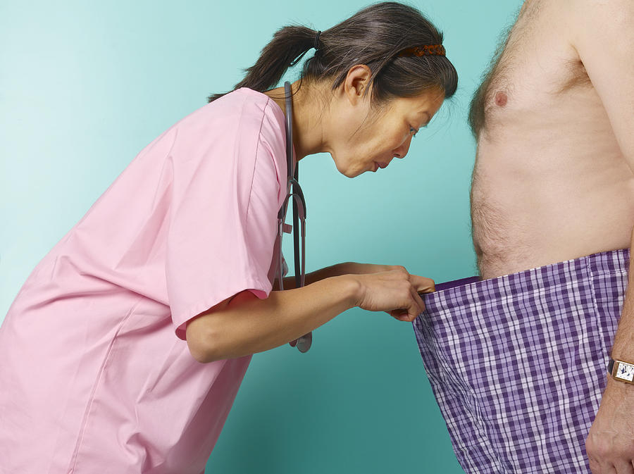 Female doctor looking down into barechested mans pants, profile Photograph by Peter Dazeley