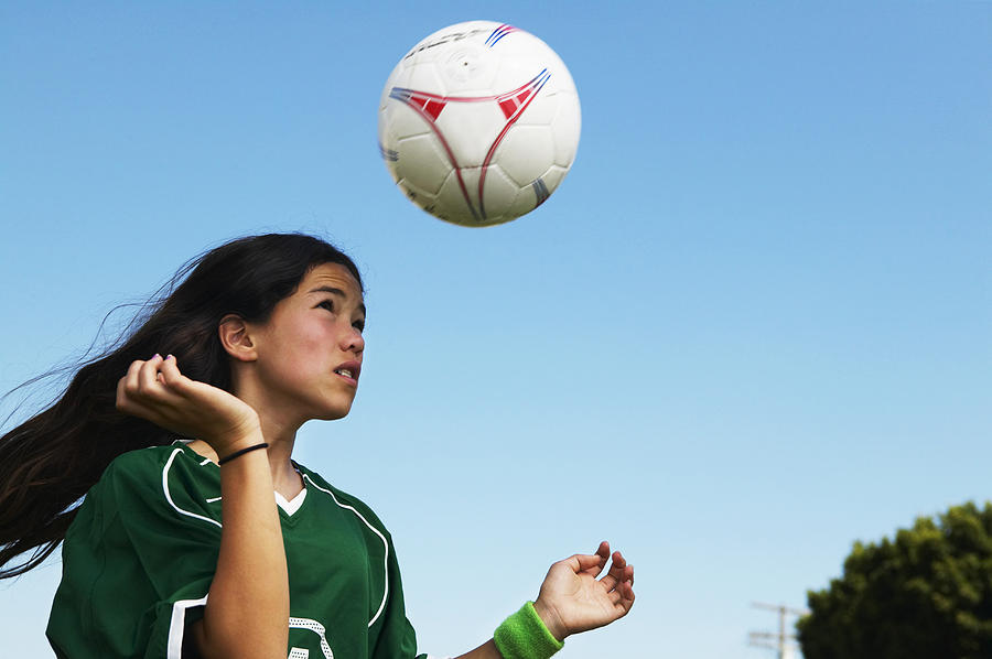 Female footballer (11-13) heading ball, low angle view Photograph by Barry Austin