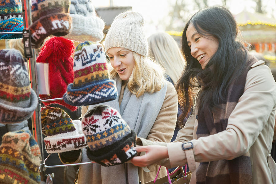 Female friends are looking at woolen hats at outdoor Christmas market stall. Photograph by Betsie Van der Meer