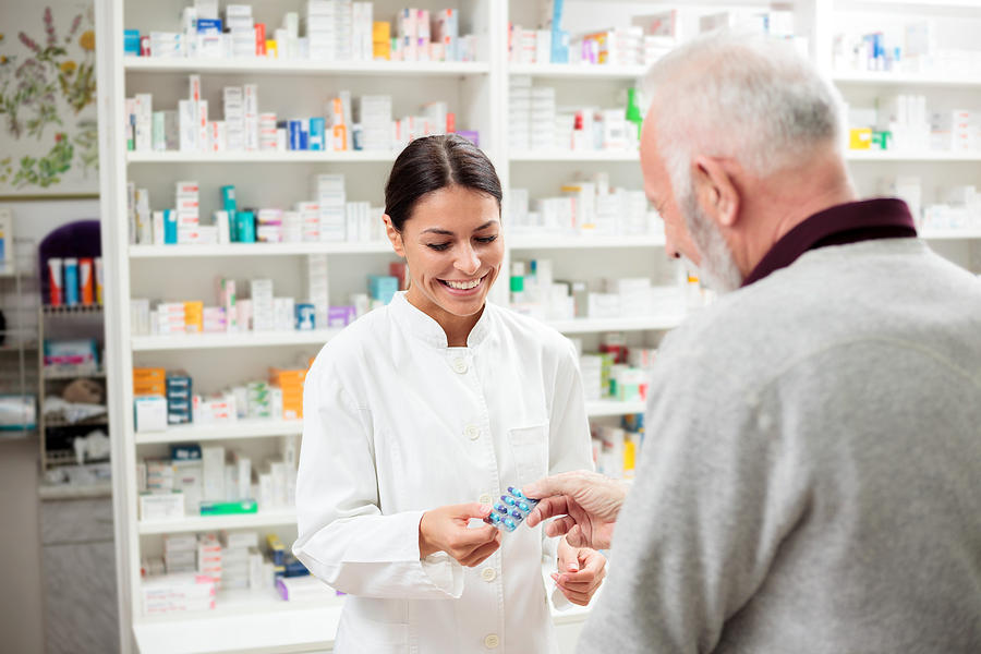 Female pharmacist giving medications to senior customer Photograph by Gligatron