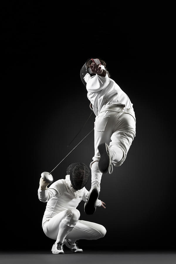 Fencers fencing, one fencer jumping in air Photograph by PhotoAlto/Milena Boniek