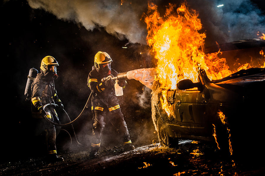 Firefighters spraying water on burning car Photograph by Simonkr