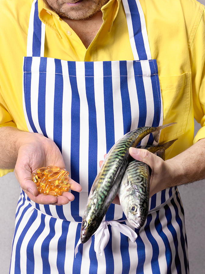 Fishmonger holding mackerel and Cod Liver oil tablets, close-up, mid section Photograph by Peter Dazeley