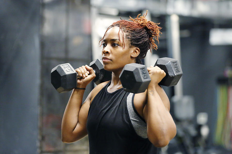 Fit, young African American woman working out with hand weights in a fitness gym. Photograph by Mireya Acierto