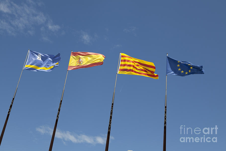 Flags of regions of Spain on flagpoles against blue sky Salou Sp Photograph by Peter Noyce