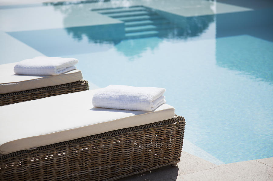 Folded towels on lounge chairs beside pool Photograph by Martin Barraud