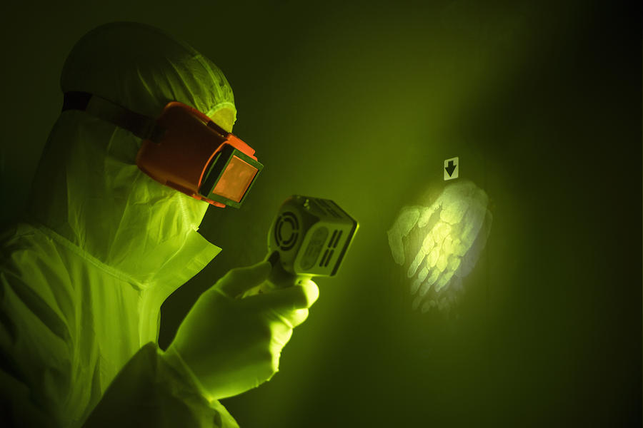 Forensic scientist using finger print light to find hand print on wall at crime scene Photograph by Monty Rakusen