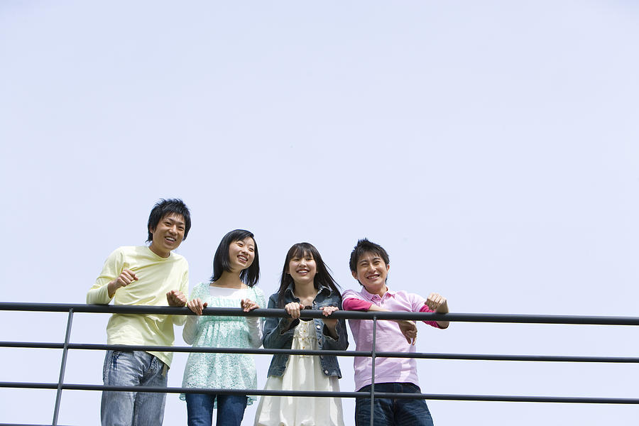 Four young people leaning on the railing, side by side, low angle view, blue background, copy space, Japan Photograph by Daj