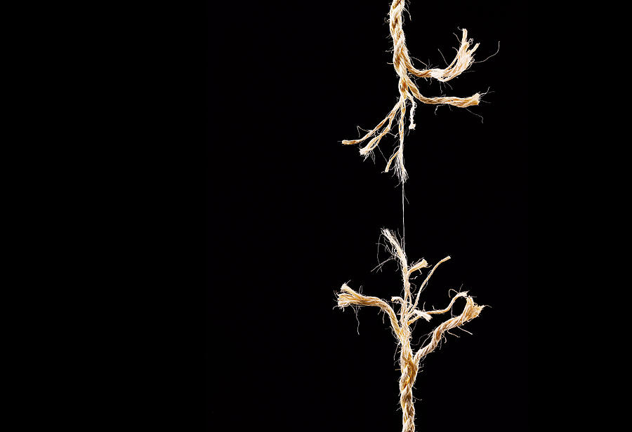 Frayed rope breaking on black background Photograph by Peter Dazeley