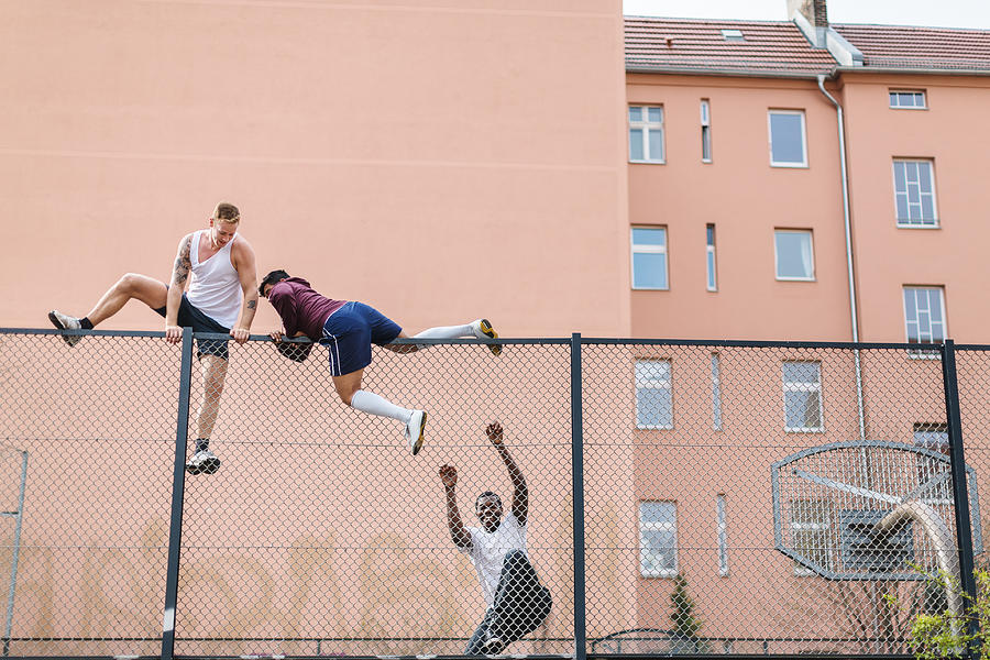 Friends Climbing Over Fence Photograph by Hinterhaus Productions