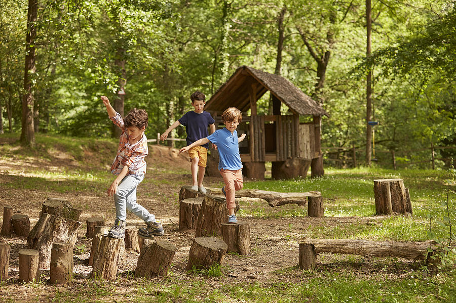 Friends playing on tree stumps in forest Photograph by Morsa Images