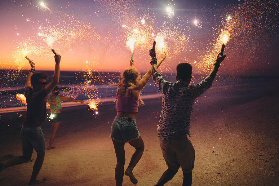 Friends running on a beach with fireworks Photograph by Wundervisuals