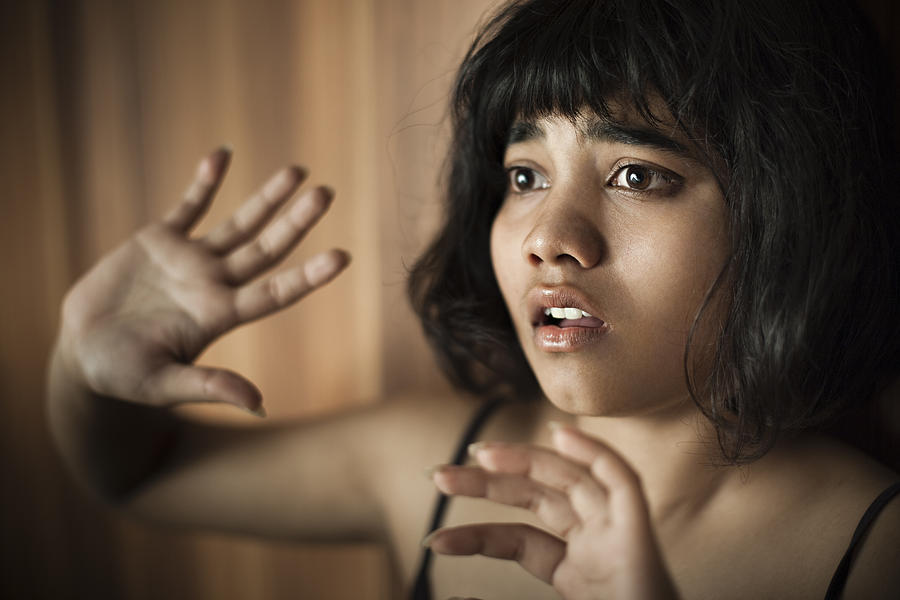 Frightened teenage girl looking away and hiding herself behind hands. Photograph by Gawrav