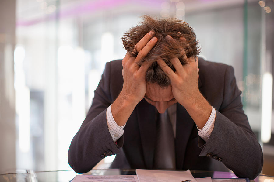 Frustrated businessman sitting at desk with  head in hands Photograph by Paul Bradbury