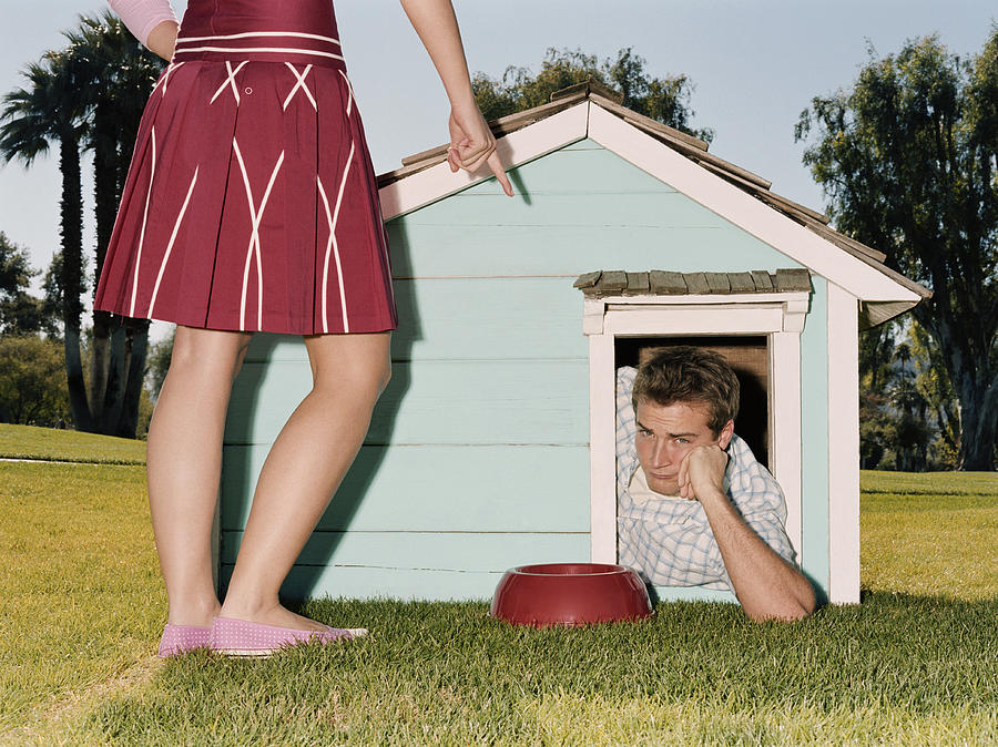 Frustrated man laying in doghouse Photograph by Deborah Jaffe