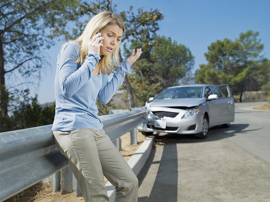 Frustrated woman using cell phone next to car wrecked on guardrail Photograph by Chris Ryan
