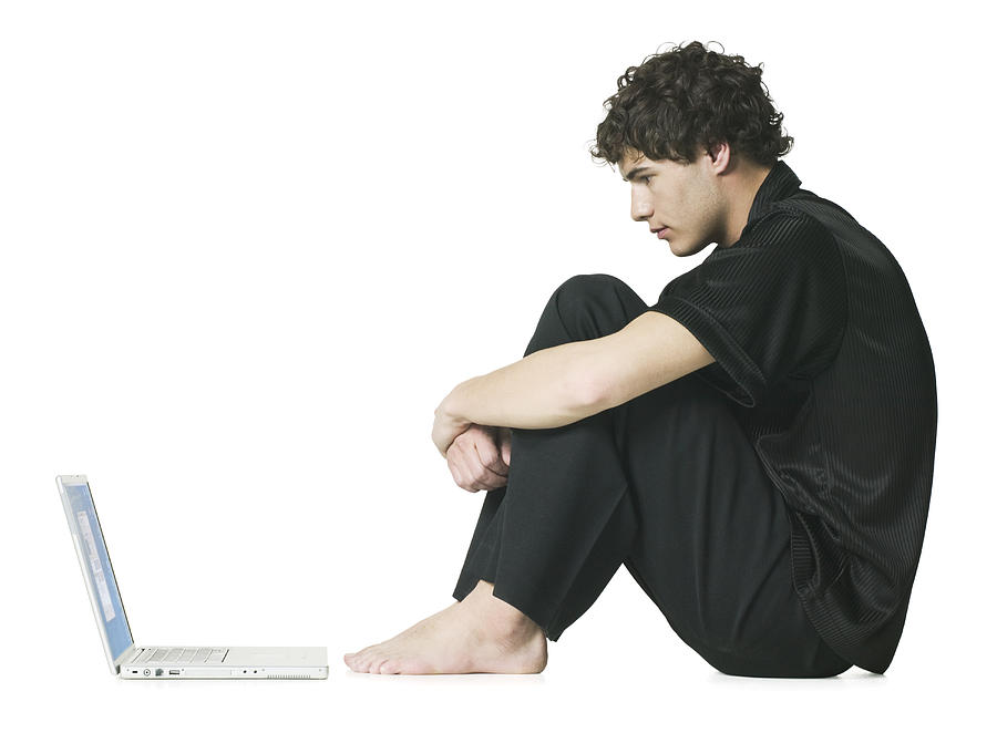 Full Body Shot Of A Teenage Male As He Sits And Stares At His Laptop Computer Photograph by Photodisc