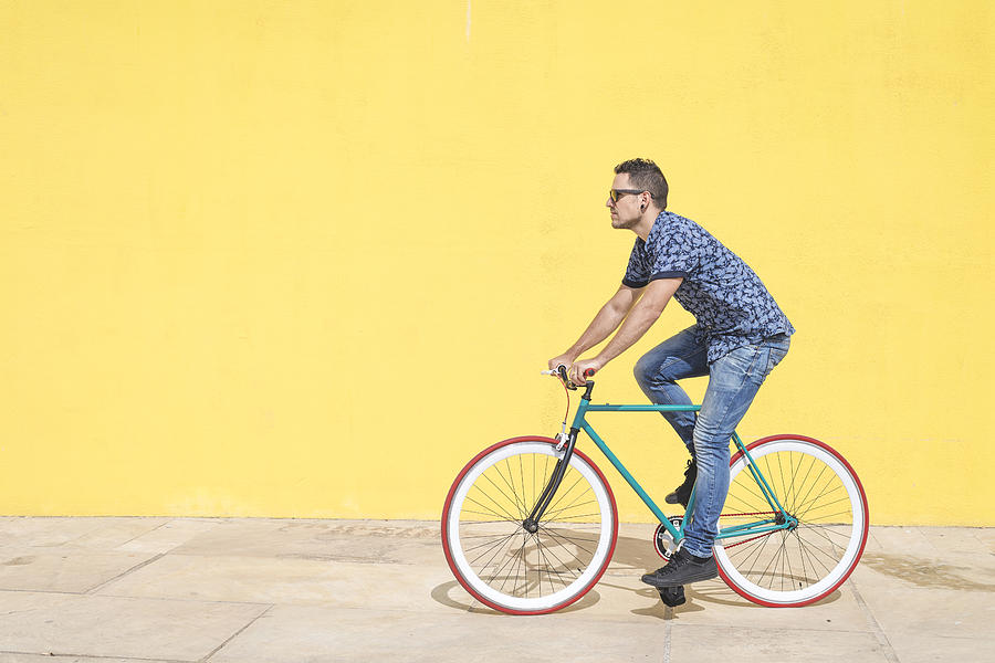Full length of man riding bicycle against yellow wall at sidewalk in city Photograph by Cavan Images