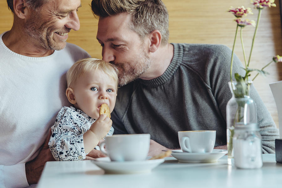 Gay couple cuddling with their baby in cafe Photograph by Westend61